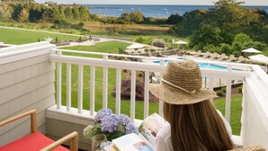 A balcony with a view of the sea, a pool, and a grassy area.