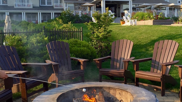A backyard with a fire pit, wooden chairs, and a house with a porch.
