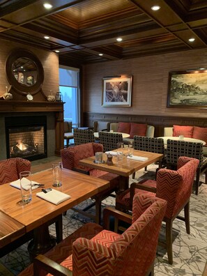 A dining area with wooden tables and patterned chairs, a fireplace, and artwork on the walls.