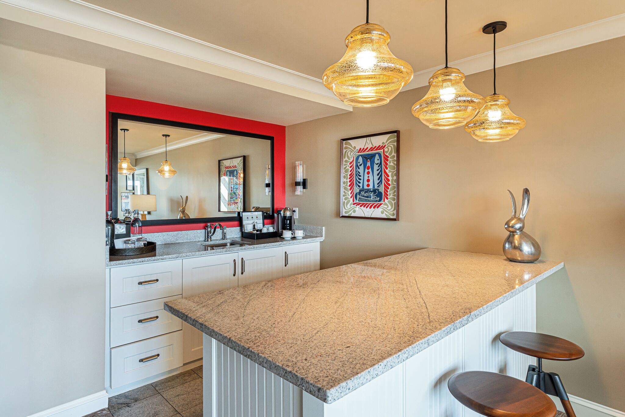Una cocina con encimera de granito, armarios blancos, pared de acento roja e iluminación colgante.