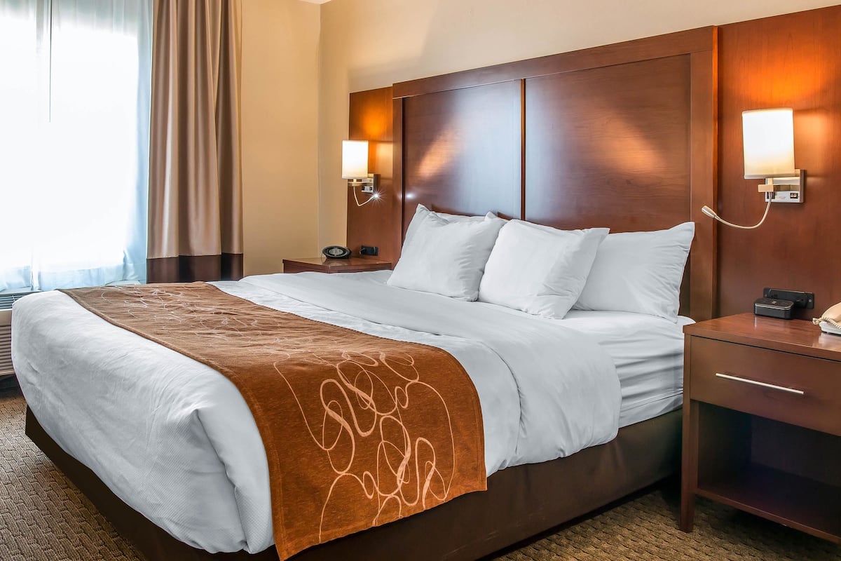 A hotel room with a large bed, two bedside tables, a nightstand, a lamp, and a window with curtains.