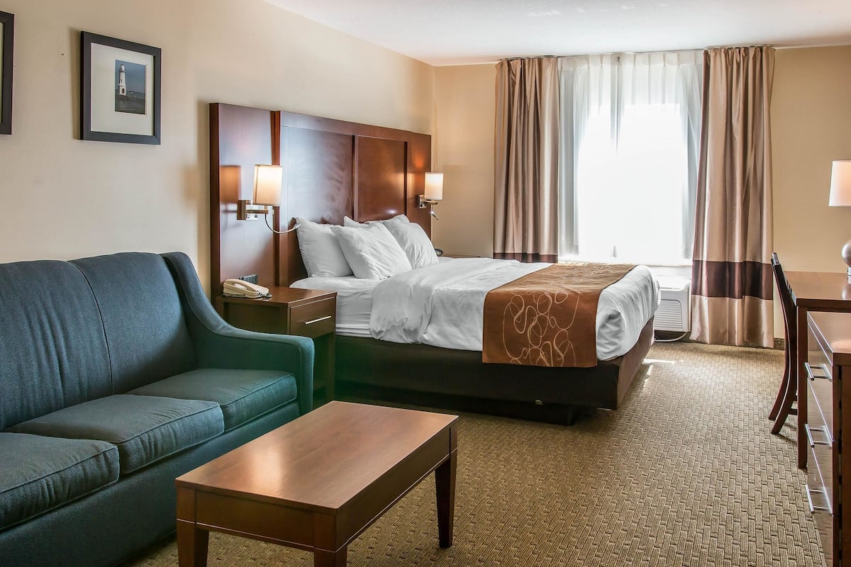 A hotel room with a bed, a sofa, a coffee table, a desk, and a lamp.