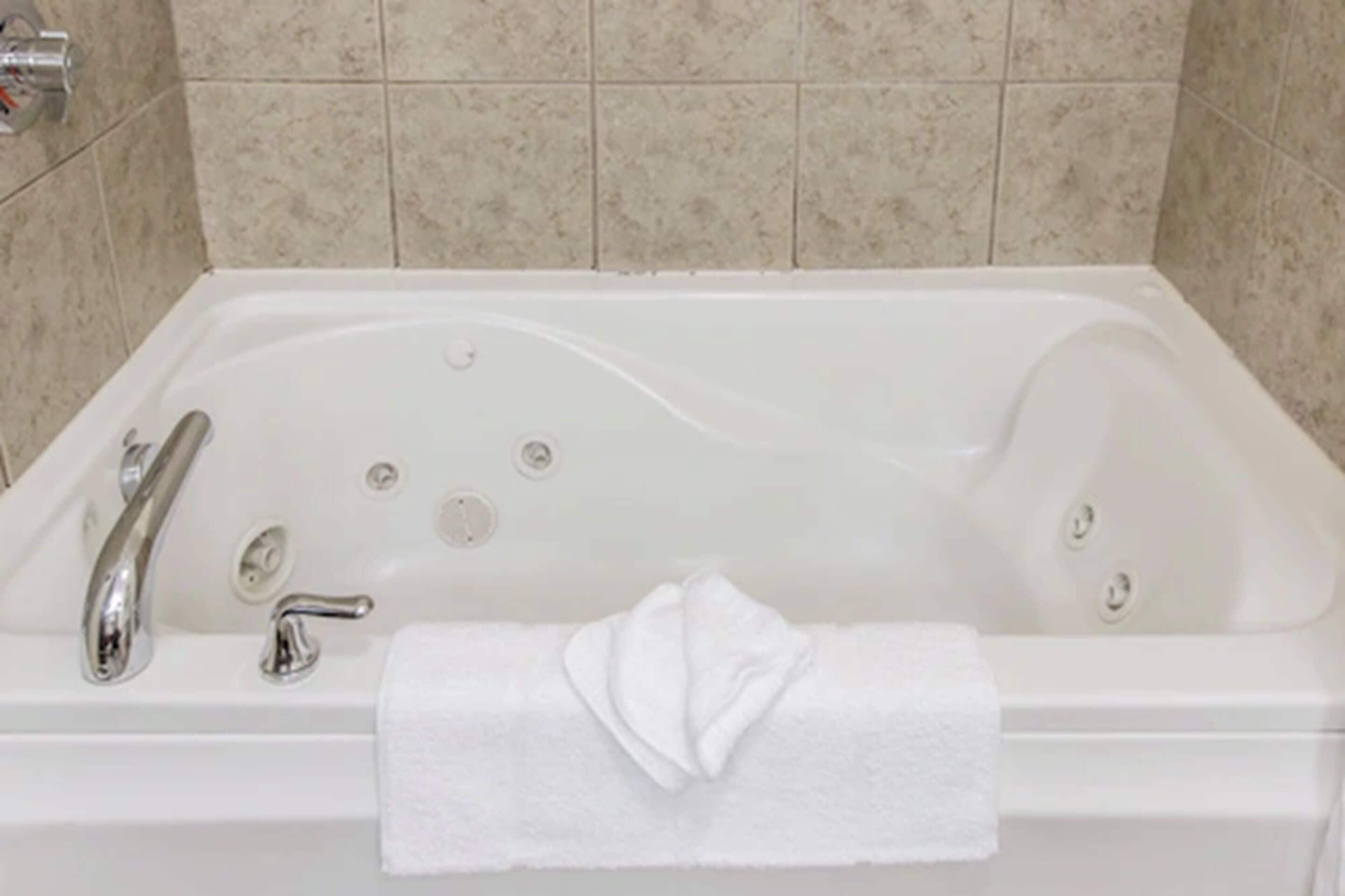 Eine weiße Badewanne mit einem Wasserhahn, einer Handbrause und einem Handtuch am Rand.
