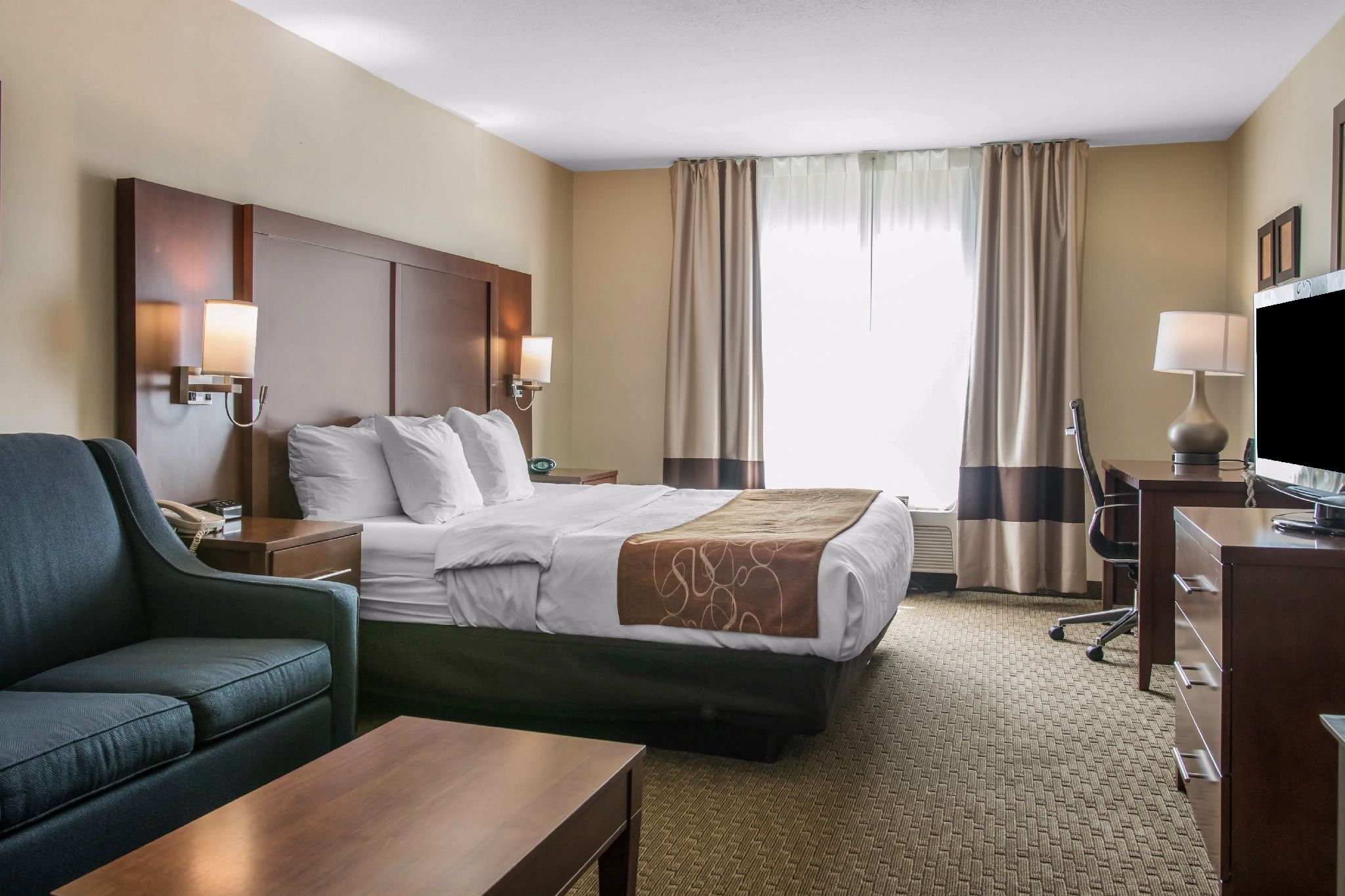 Una habitación de hotel con cama, escritorio, silla, sofá, televisor y lámpara.