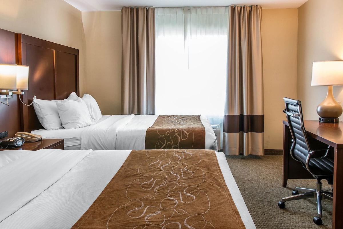 A hotel room with two beds, a desk, and a chair.