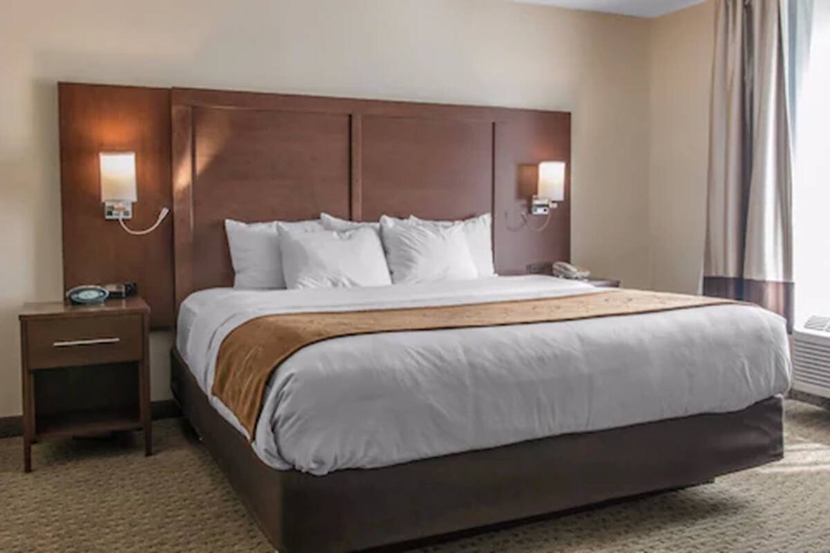A hotel room with a large bed, two bedside tables, a nightstand, and a wall-mounted telephone.