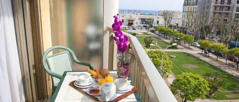 Un balcón con una mesa dispuesta para el desayuno, con vistas a un paisaje urbano que incluye edificios y un parque verde.