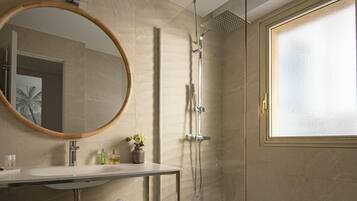 Un baño moderno con un espejo redondo grande, una ducha con cabezal de lluvia y un ventanal con cristal satinado.