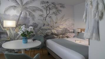Una habitación con cama, una mesa redonda con sillas, una lámpara y un mural en la pared.