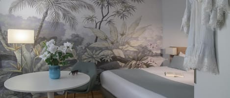 A room with a bed, a round table with chairs, a lamp, and a wall mural.