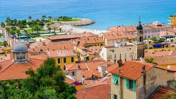 A coastal town with terracotta-roofed buildings, a prominent church with a dome, and a beach area with palm trees.