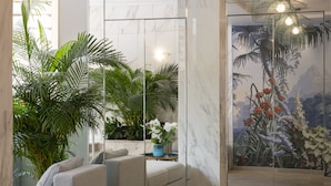 A modern interior with a sofa, a blue vase with white flowers, and a mural of tropical plants. - Hotel Chambord (Menton)