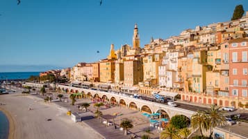Un paysage urbain côtier avec une tour imposante, une plage avec des parasols et une promenade bordée de boutiques.
