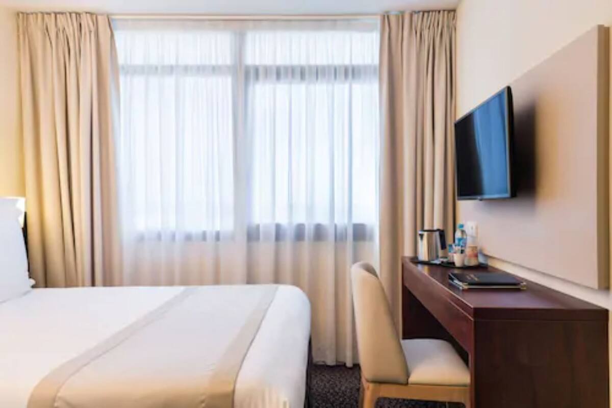 A hotel room with a bed, a desk with a chair, a television, and a window with curtains.