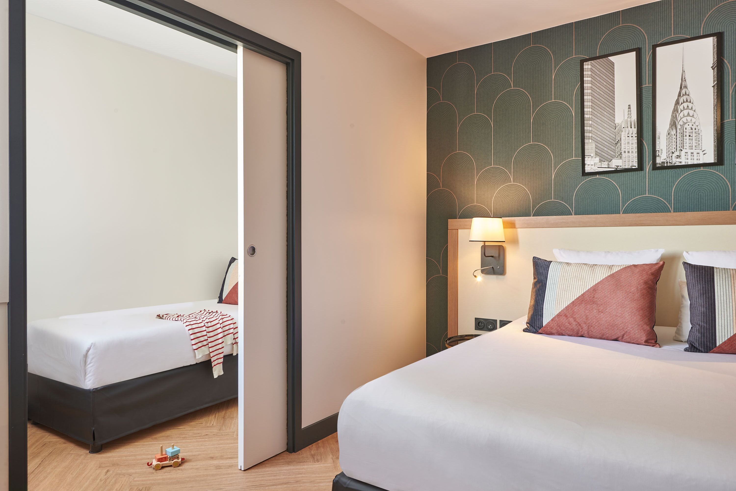 A hotel room with a large bed, a smaller bed, a mirror, and a wall with framed pictures.