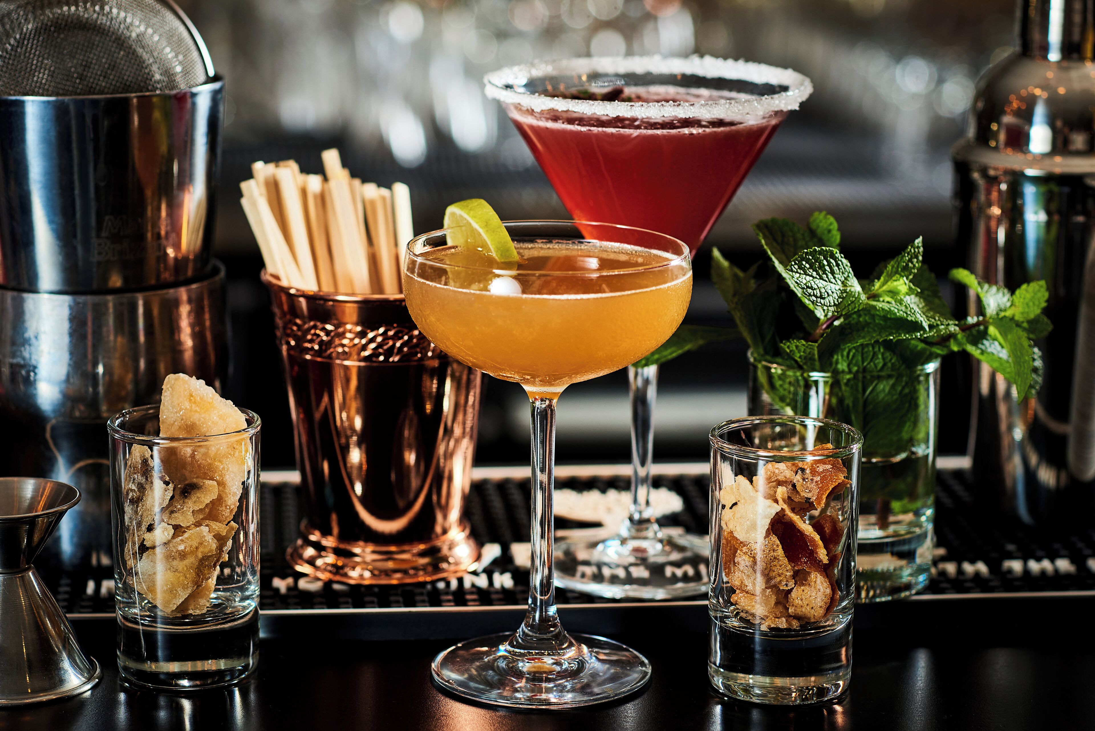 A bar setting with various drinks, a cocktail shaker, and a copper mug.