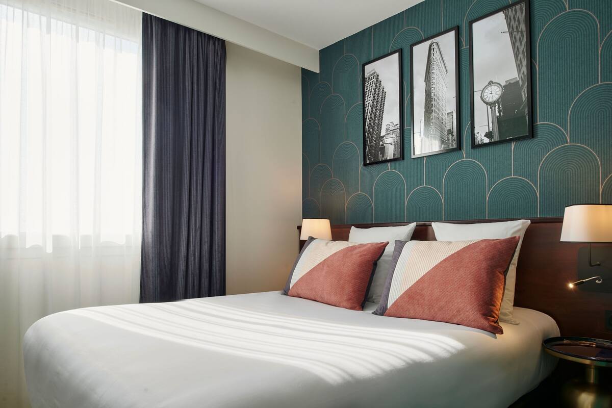 A hotel room with a large bed, a nightstand with a lamp, and three framed pictures on the wall.