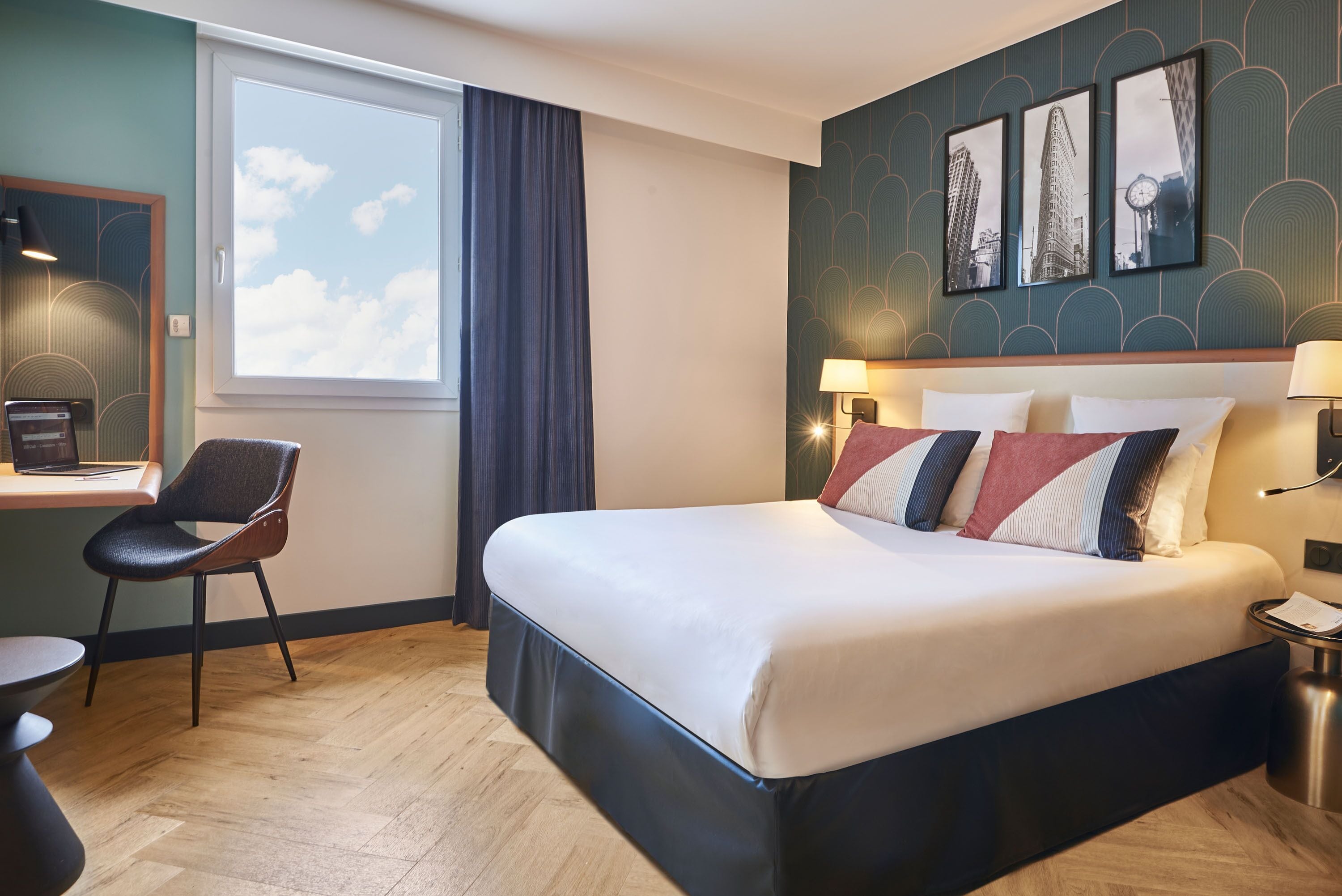 Habitación de hotel con una cama grande, un escritorio con silla, una ventana con cortinas y cuadros en la pared.