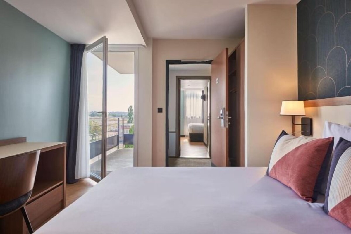 Quarto de hotel com uma cama, uma mesa e vista para o exterior.