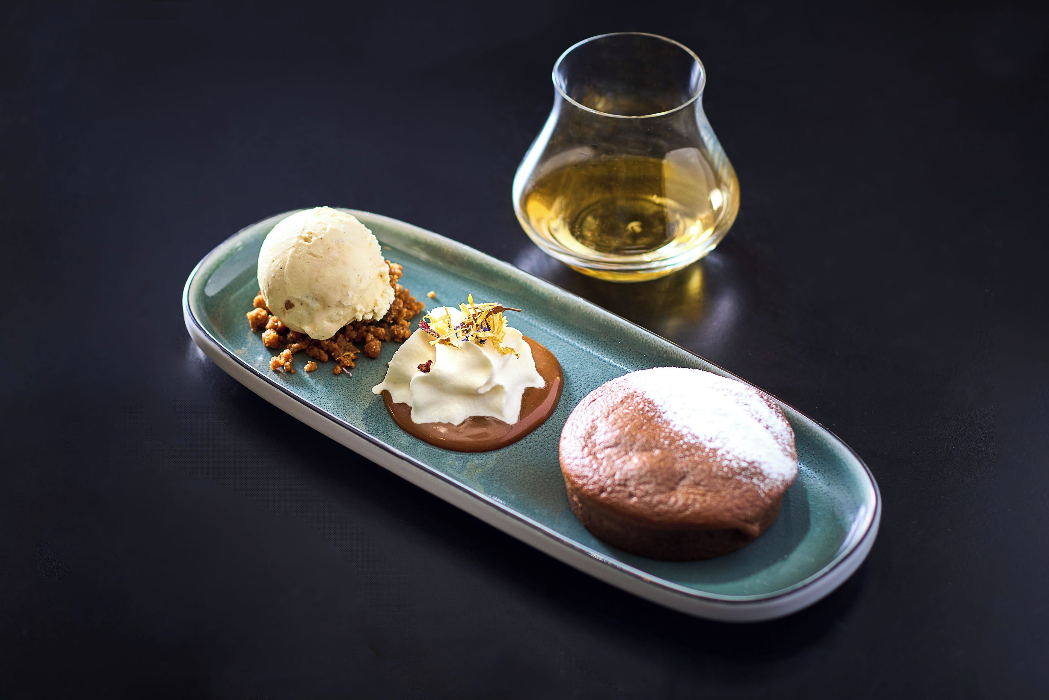 A dessert plate with ice cream, whipped cream, and a pastry on a teal plate.