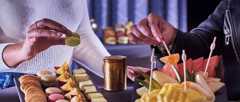 A table with various food items including macarons, cheese, fruits, and a chocolate bar.