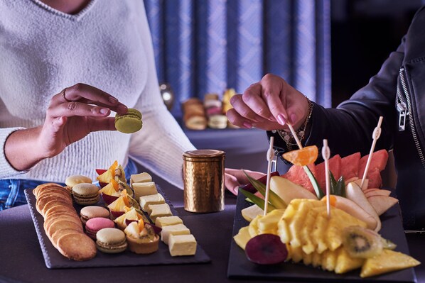 A table with various food items including macarons, cheese, fruits, and a chocolate bar.