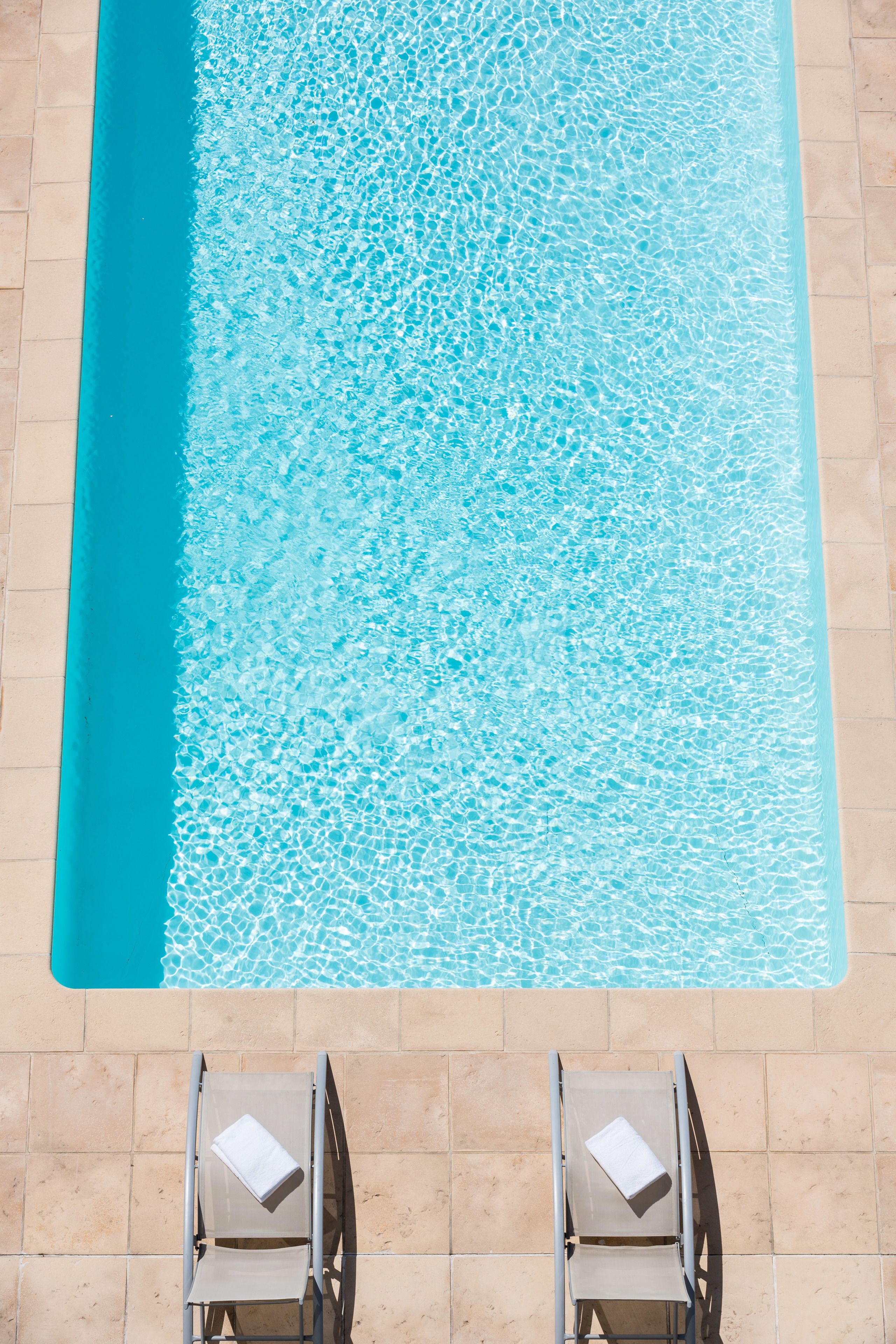 A swimming pool with two sun loungers, each with a towel.