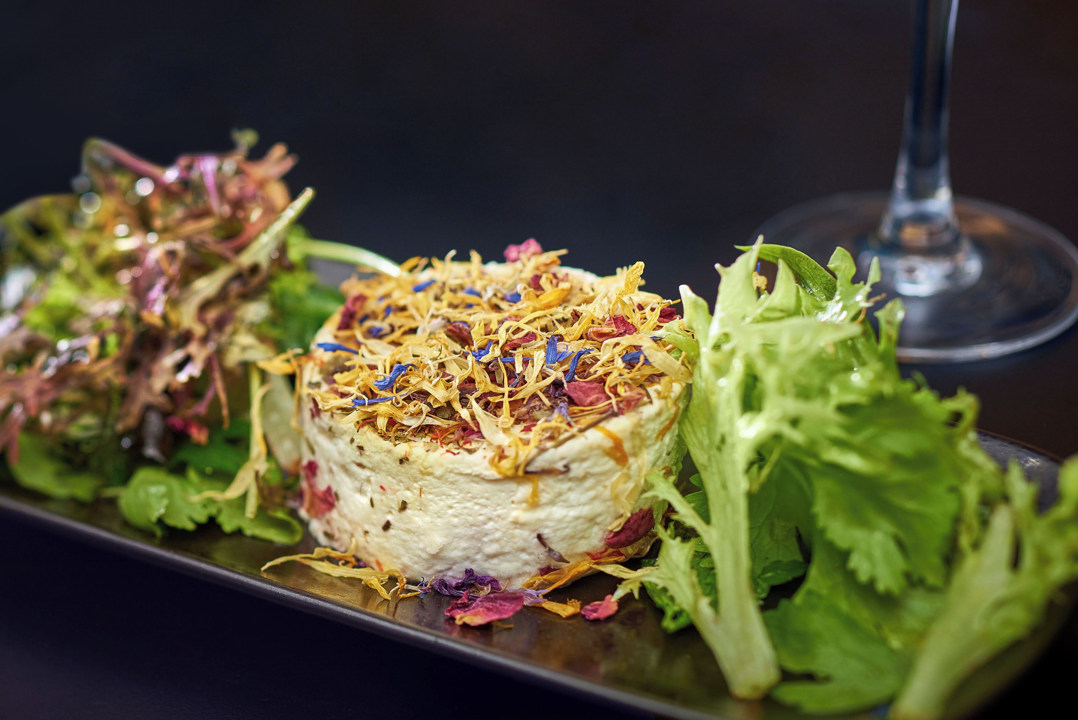 A plated dish with a variety of greens and shredded toppings, accompanied by a glass of wine.