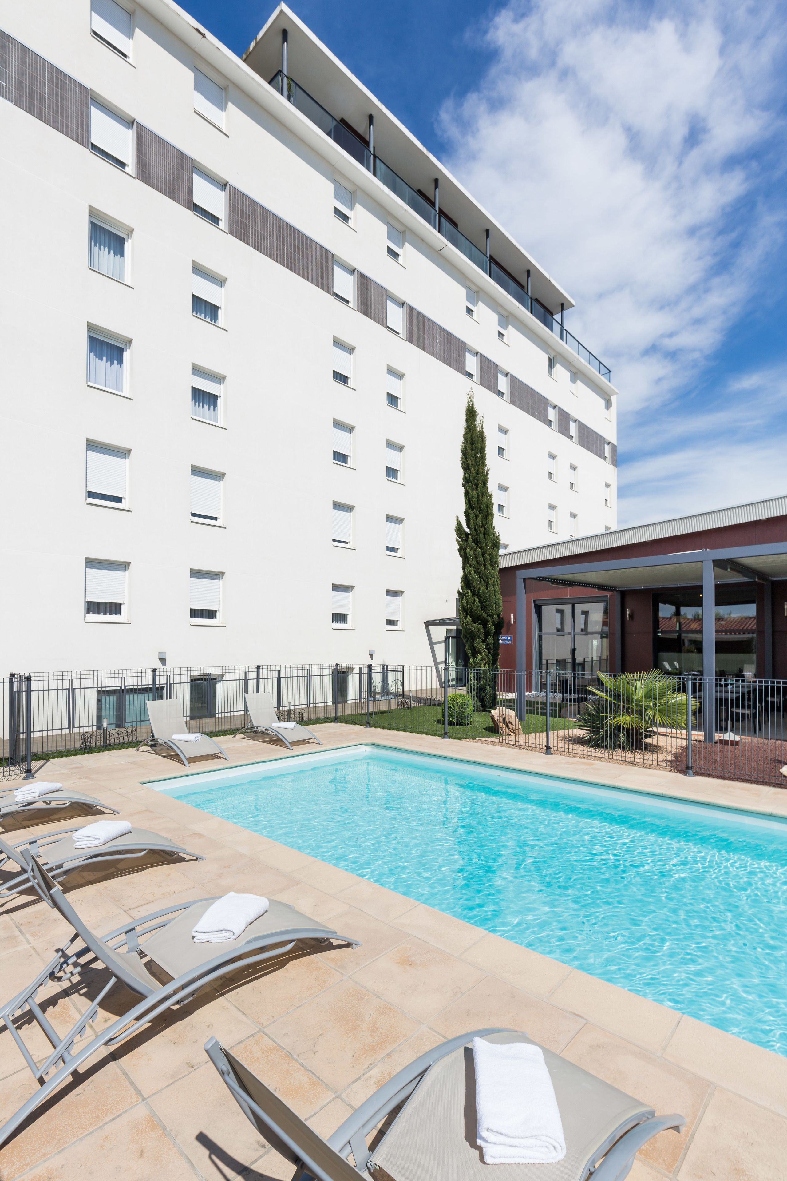 A hotel with a swimming pool, sun loungers, and a covered outdoor area.