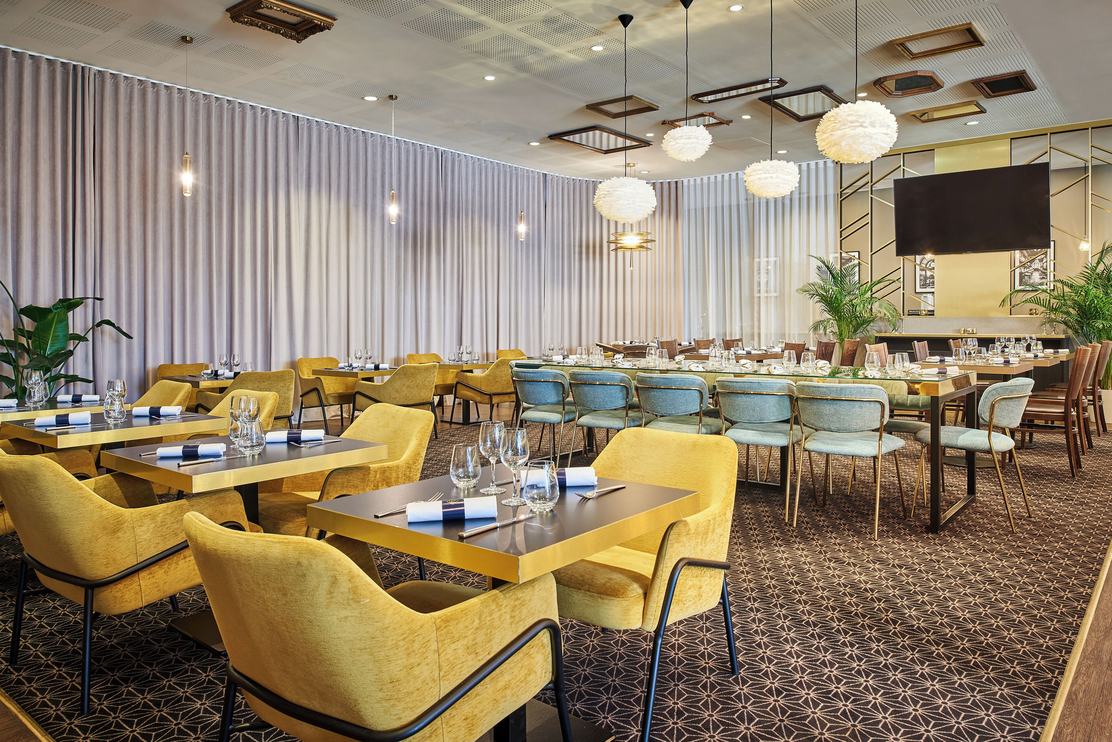 A hotel dining area with multiple tables and chairs, a large screen, and decorative lighting.