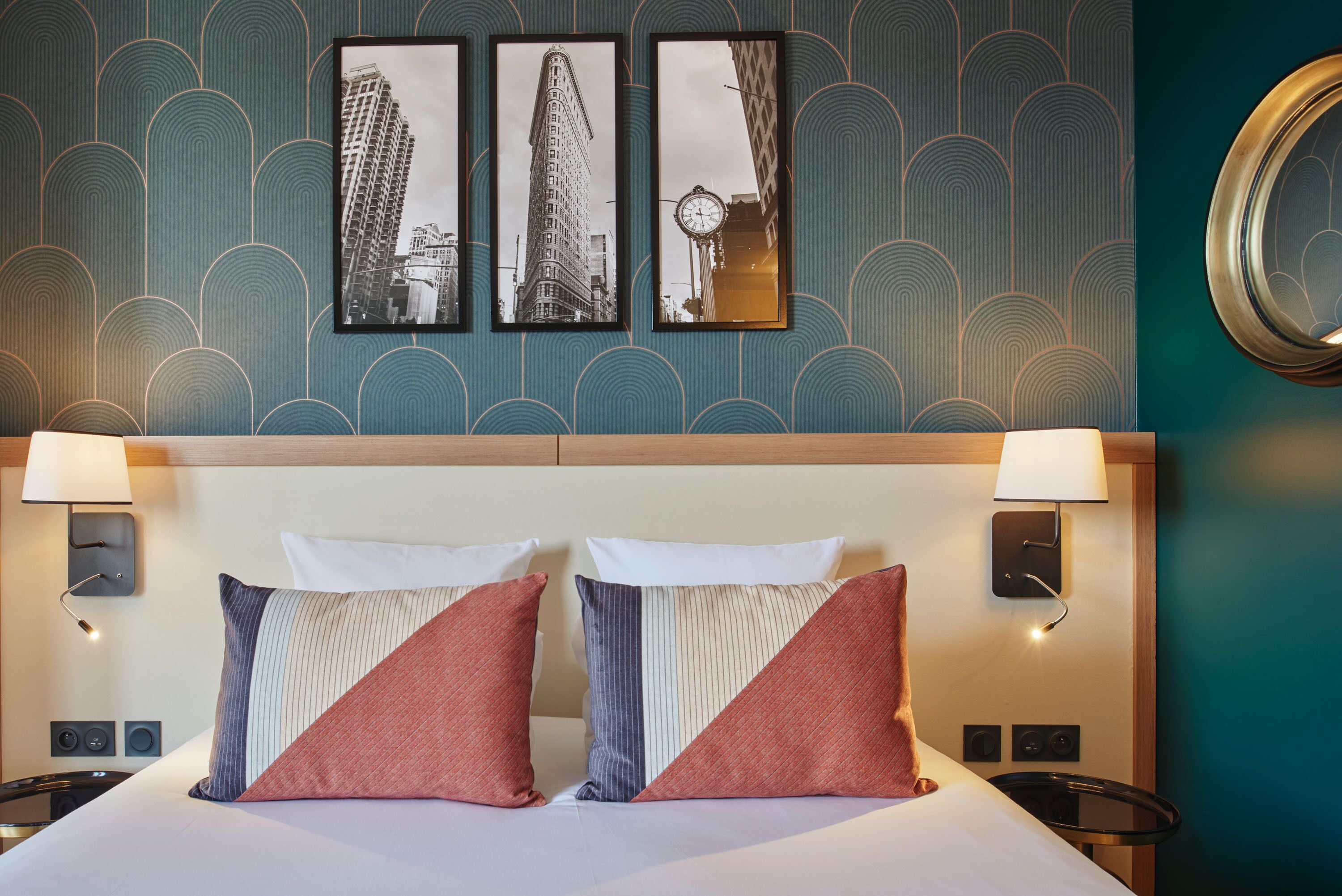 Una habitación de hotel con una cama, dos lámparas de noche, un reloj y tres cuadros en la pared.