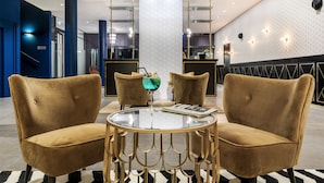 Un moderno vestíbulo de hotel con una mesa redonda central, dos sillones cómodos y un jarrón de cristal decorativo.