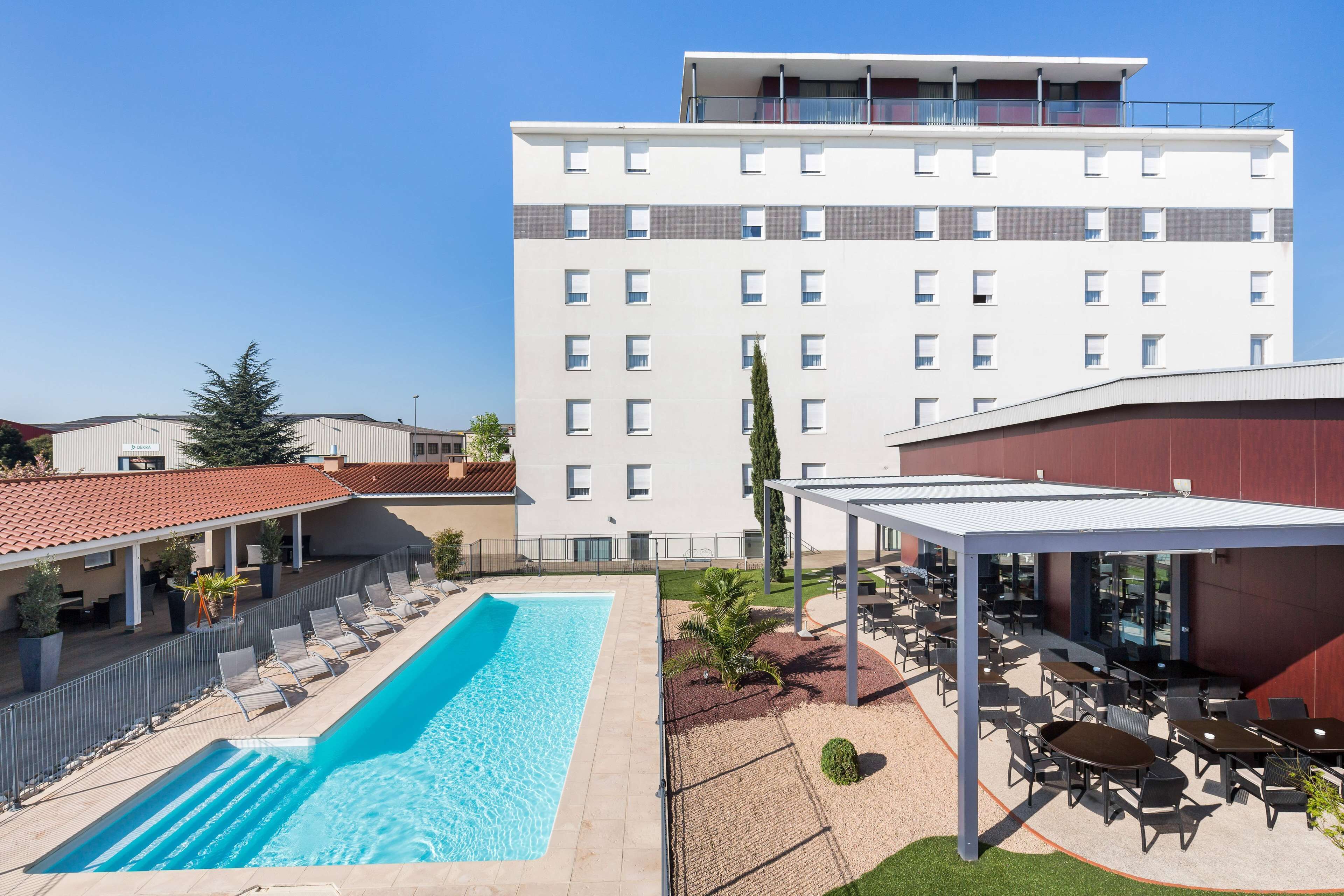 Un hotel con piscina, zona de estar al aire libre y un edificio de varios pisos con balcones.
