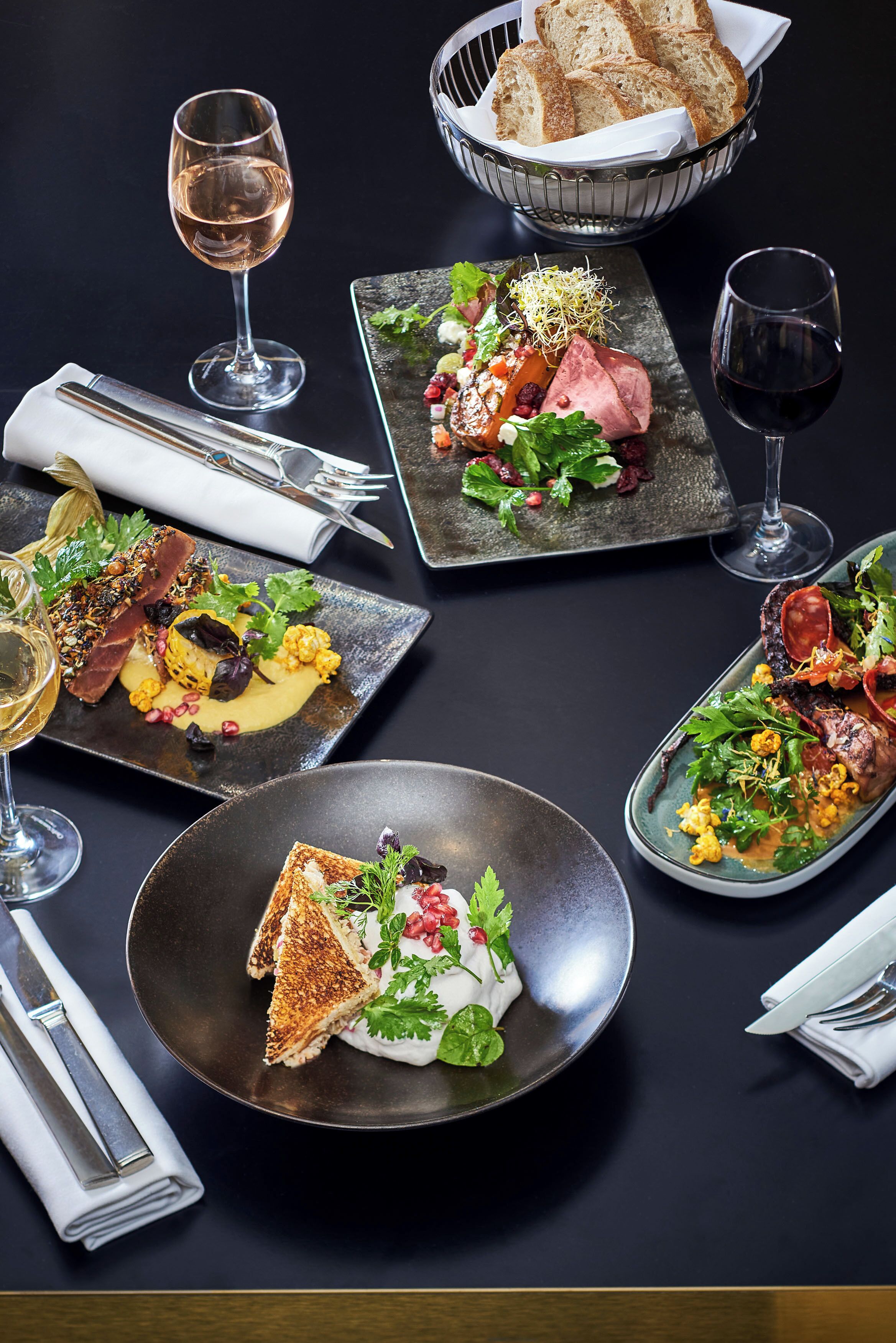 A table set with various dishes, including a salad, a steak, and a plate of toast, along with wine glasses.