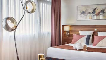 Une chambre d’hôtel avec un lit, une table de chevet avec une lampe, un tableau au mur et une fenêtre avec des rideaux.
