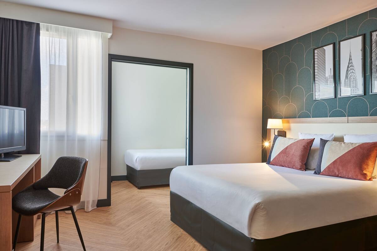 A hotel room with a bed, a desk, a chair, and a television.