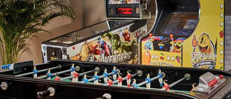 A foosball table with a digital scoreboard and a Pac-Man machine in the background.