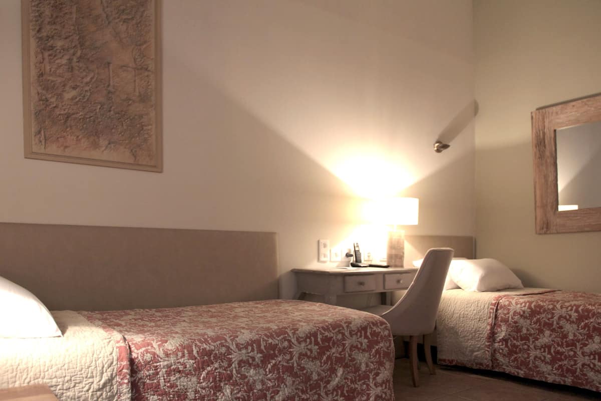 A hotel room with two beds, a desk with a lamp, a chair, and a large painting on the wall.