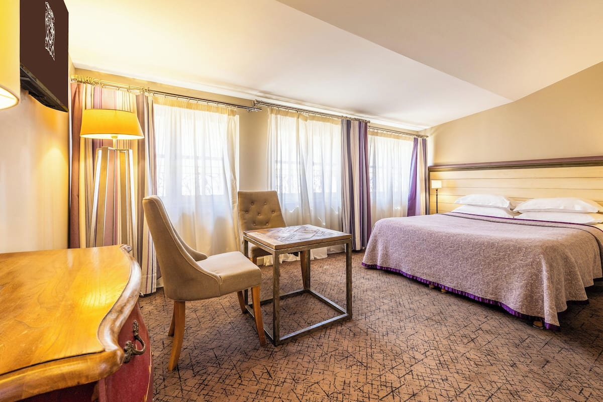 A hotel room with a bed, a desk, a chair, and a lamp.