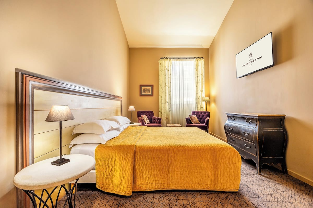 A hotel room with a large bed, a small round table, a dresser, and a framed sign on the wall.