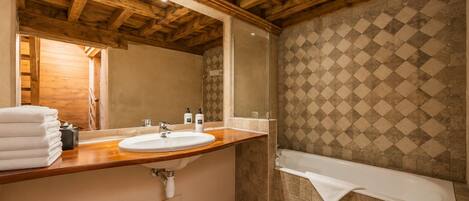 A bathroom with a wooden ceiling, a sink, a mirror, a bathtub, and a patterned wall.