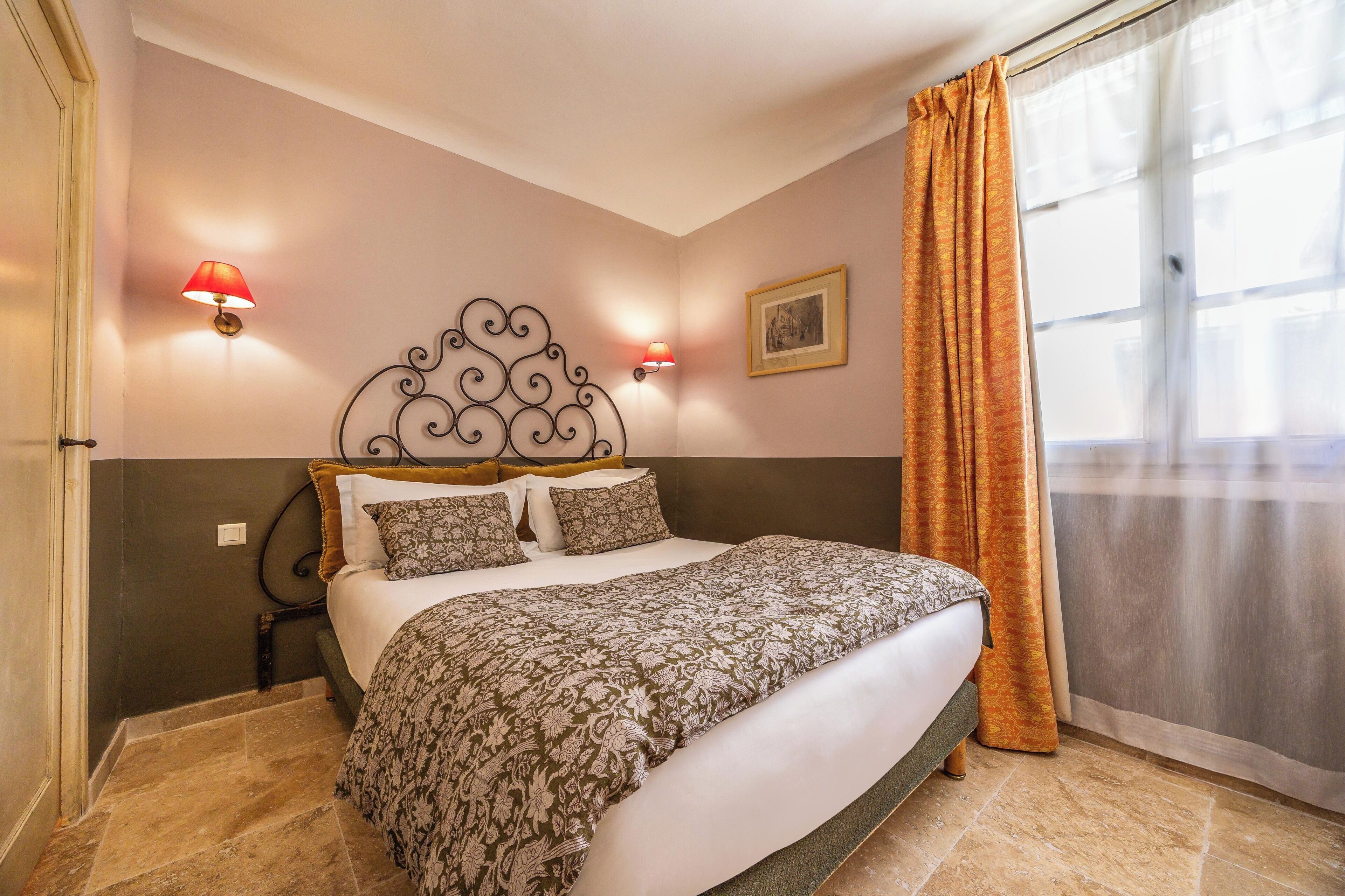 A bedroom with a bed, two wall-mounted lamps, a framed picture, and a window with curtains.