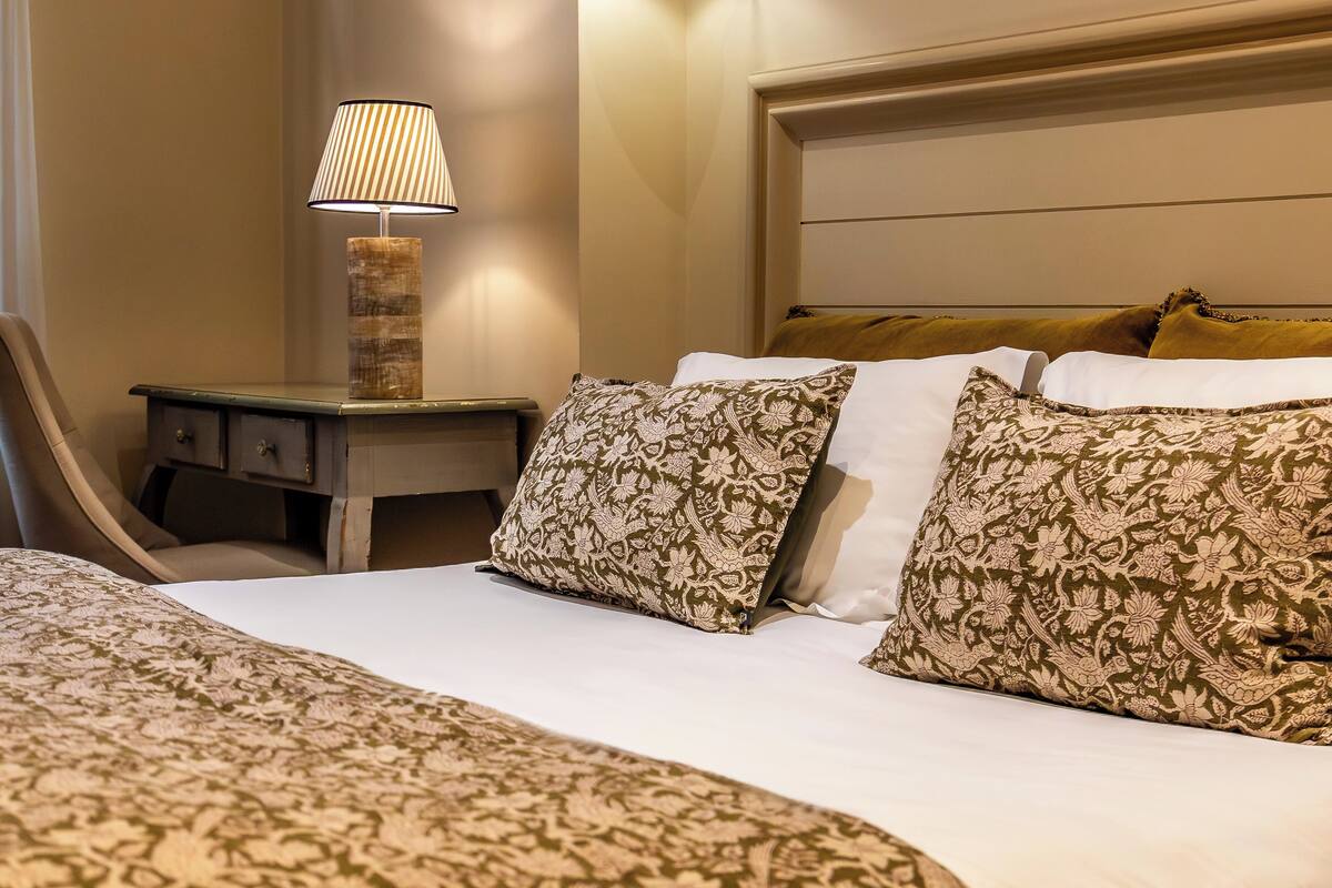 A neatly made bed with patterned bedding, a bedside lamp, and a headboard with decorative pillows.