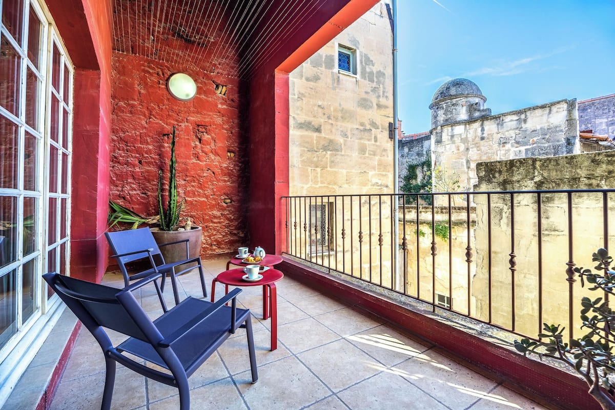 A balcony with a red wall, a potted plant, a table with cups, and a chair.