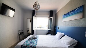 A hotel room with a bed, a window, a painting, a TV, and a towel rack. - Bel Azur (Six-Fours-les-Plages)