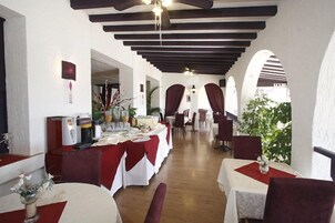 Un restaurant aux murs blancs, aux nappes rouges et aux poutres en bois au plafond. Les tables sont dressées avec des nappes blanches et des chemins de table rouges.