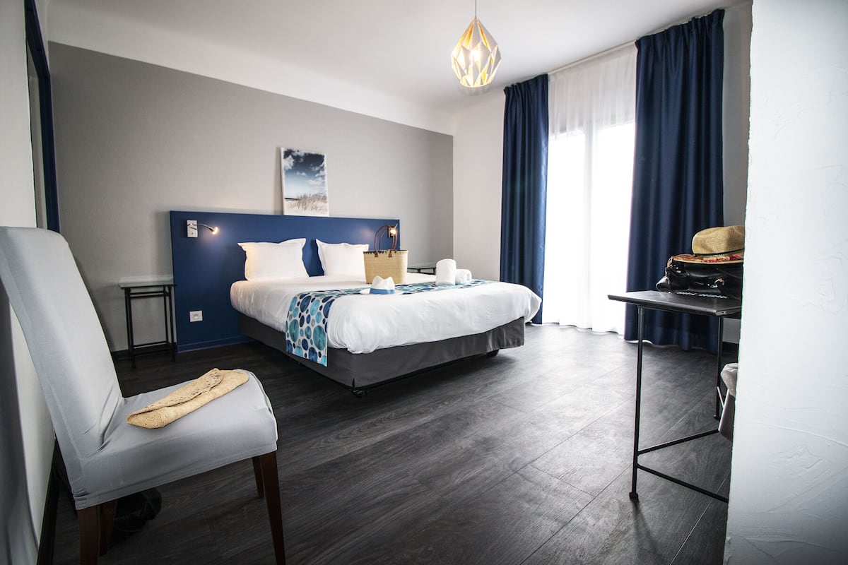 A modern hotel room with a large bed, a desk, a chair, and a view of the outdoors.
