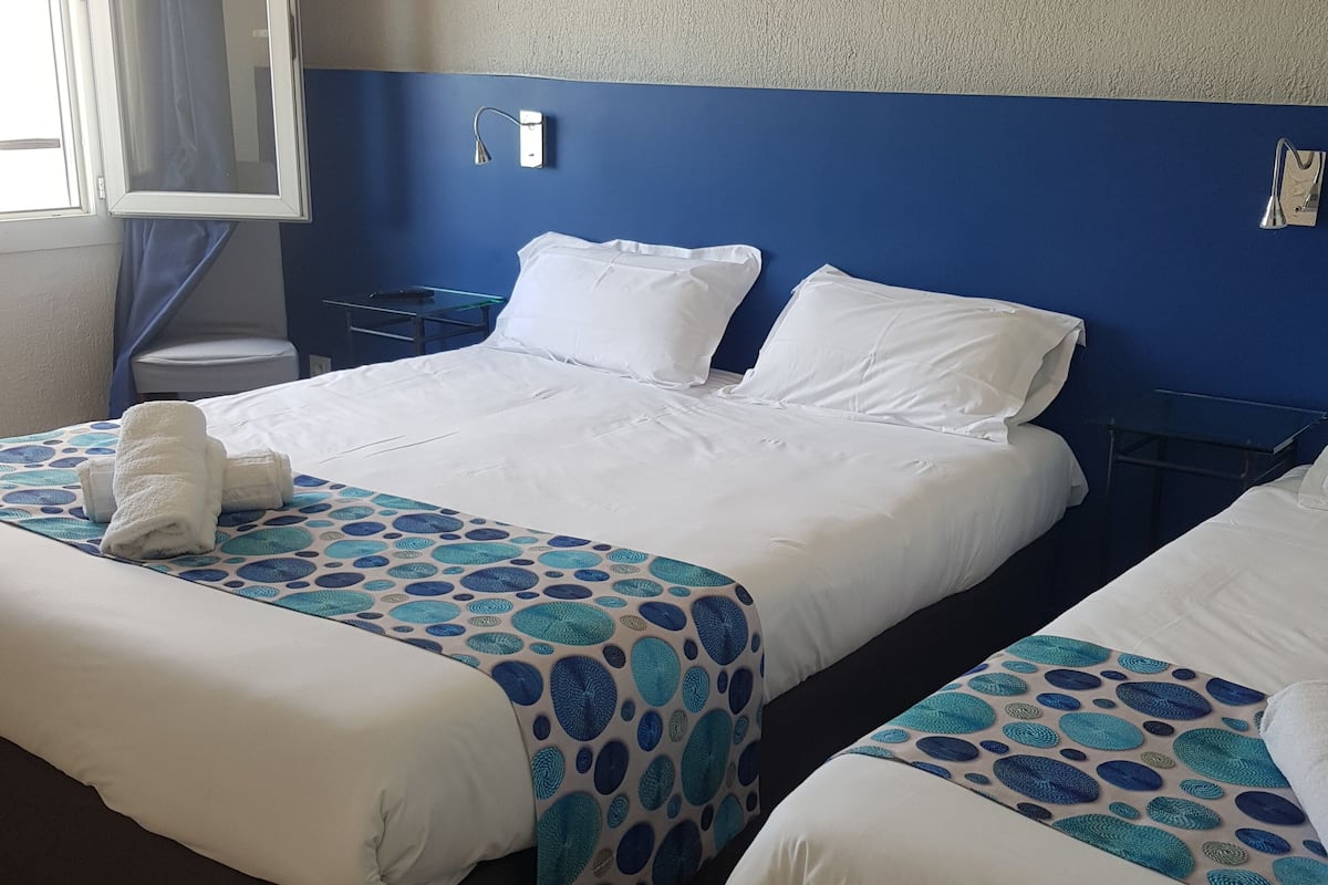 A hotel room with two beds, a painting of a beach, and a window with curtains.