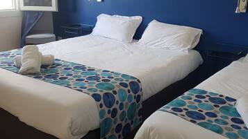 A hotel room with two beds, a painting of a beach, and a window with curtains.