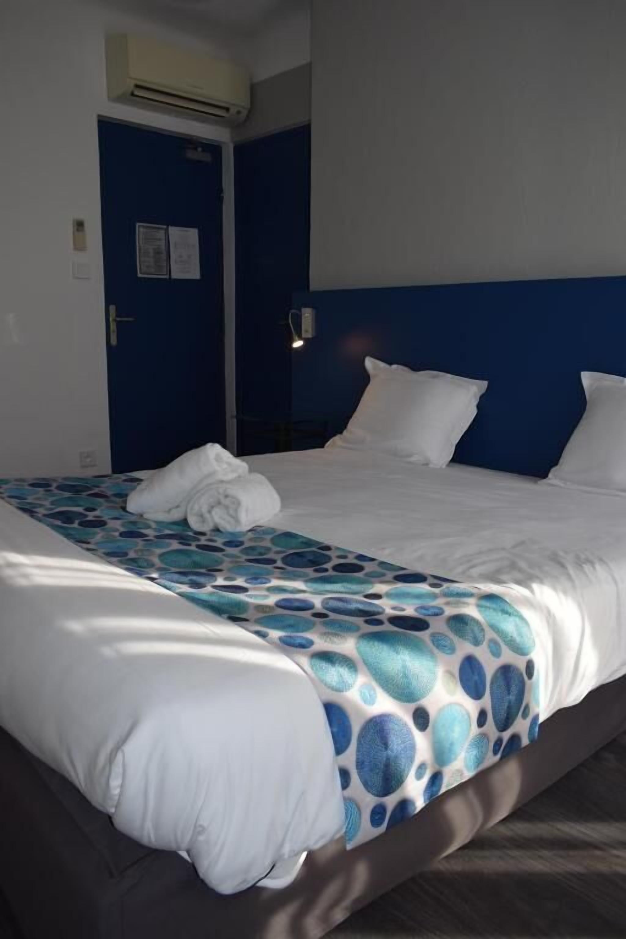 Une chambre d’hôtel avec un lit, une tête de lit bleue et un couvre-lit blanc.
